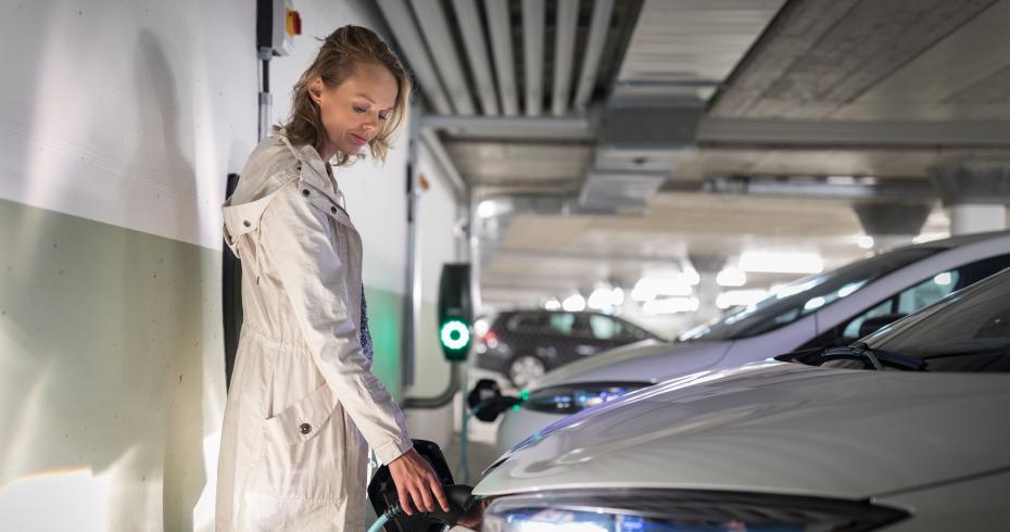 vrouw staat haar auto te laden in een overdekte parkeergarage
